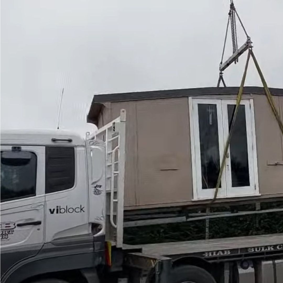 A small house structure is being lifted onto a flatbed truck by a crane, labeled "viblock," as part of embracing change.