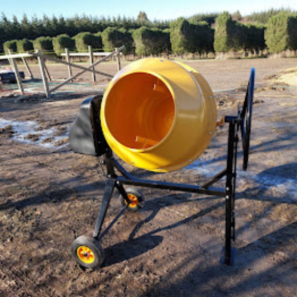 A yellow concrete mixer stands on a dirt ground with a backdrop of trees and a fenced area, symbolizing growth and embracing change in the midst of nature's renewal.