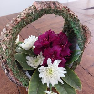 A charming ring-shaped, rustic wooden floral arrangement featuring white chrysanthemums and vibrant red flowers graces the table, capturing the essence of Rhodo Direct's Home Page aesthetic.