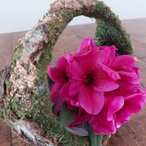 A Rhodo Direct pink flower arrangement sits beautifully in a rustic, moss-covered basket on a wooden table, bringing an elegant touch to any home page setting.