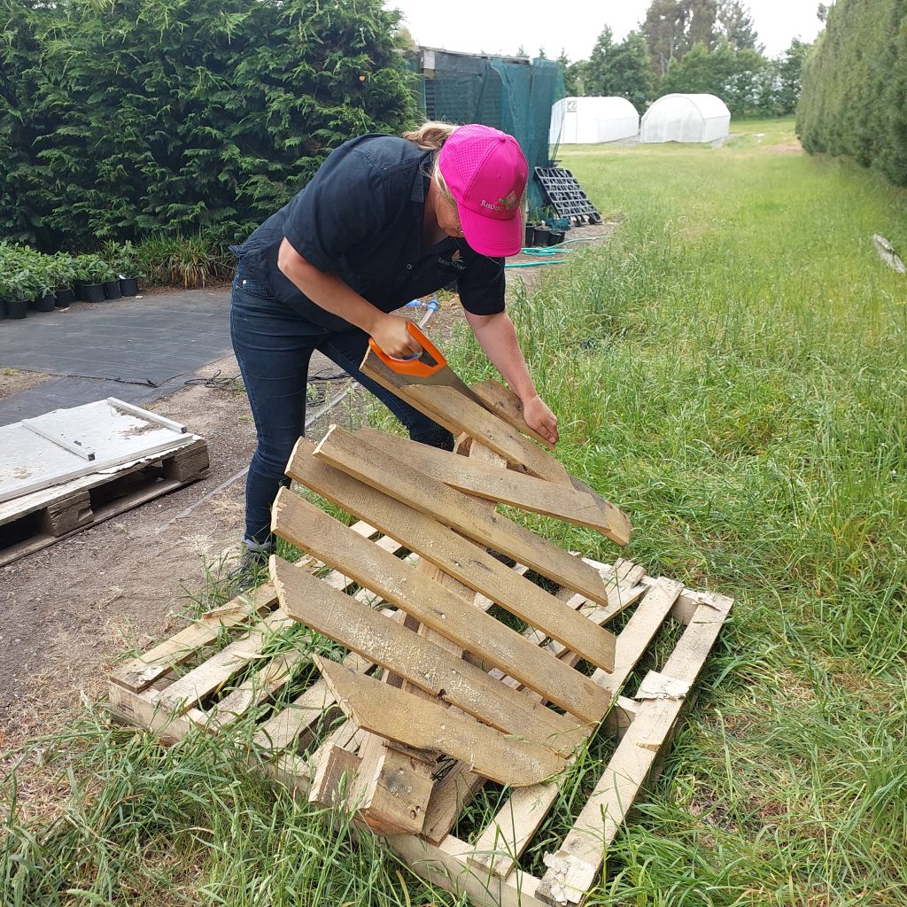 In the garden, surrounded by grass and trees, a person is getting into the Christmas spirit by skillfully cutting a wooden pallet with a hand saw, perhaps crafting festive decorations for the holiday season.